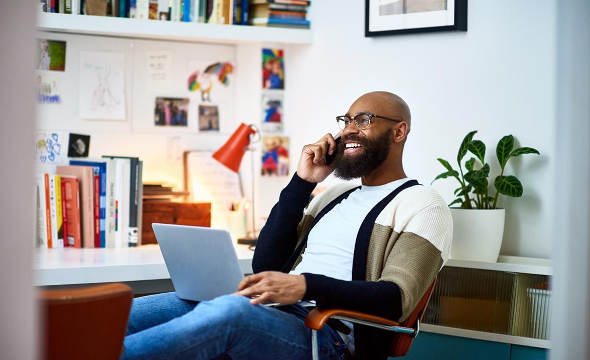 A man sits at a computer talking on the phone